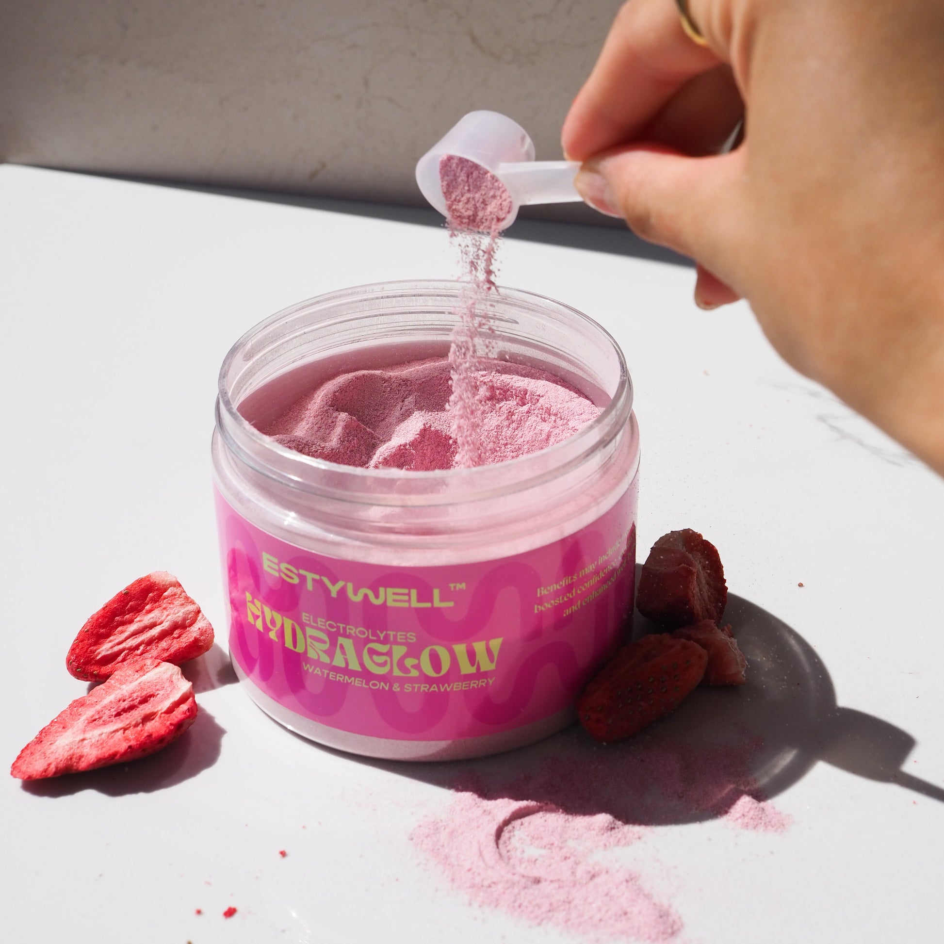 Estywell Hydraglow elektrolyty s melónovou a jahodvou príchuťou – detail otvoreného balenia s odmerkou.